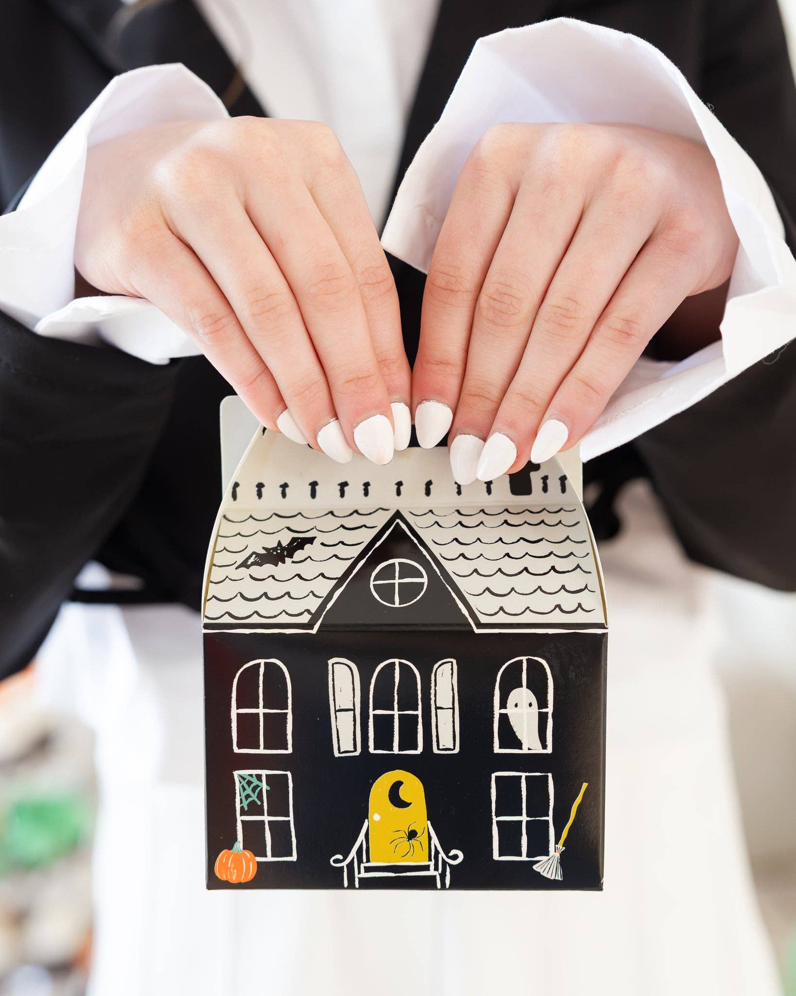 Halloween-themed treat box held by a person with white nail polish.