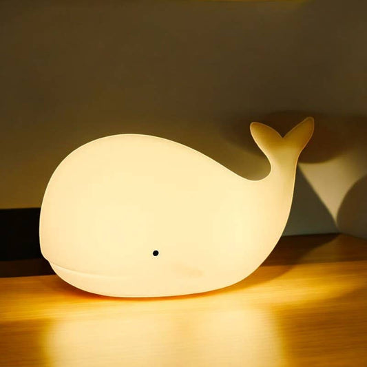 Whale-shaped night light on a wooden surface with a dark background