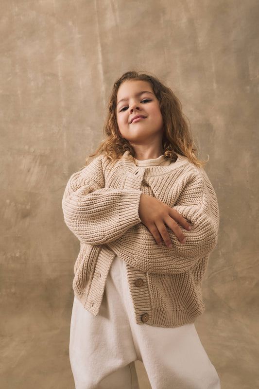 Young girl wearing a beige knitted cardigan against a textured brown background