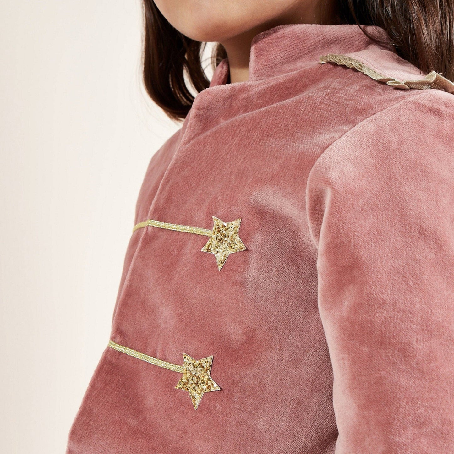 Close-up of a pink velvet jacket with gold star details on a neutral background