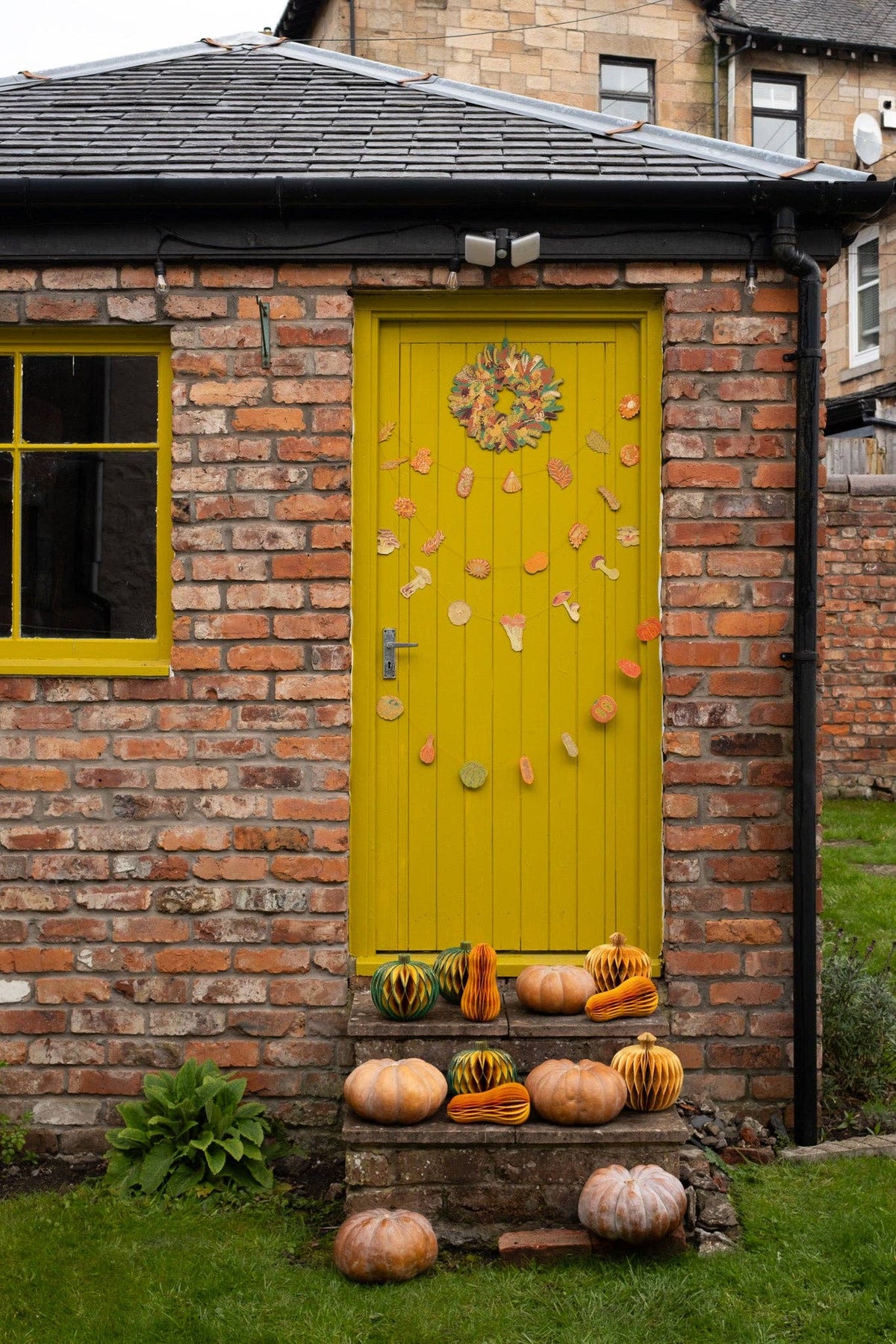 Mushroom paper garlands hanging on a yellow door above steps decorated with pumpkins and paper gourds.