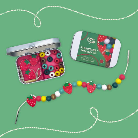 two strawberry bracelet gift kit tins and a beaded strawberry bracelet on a green background