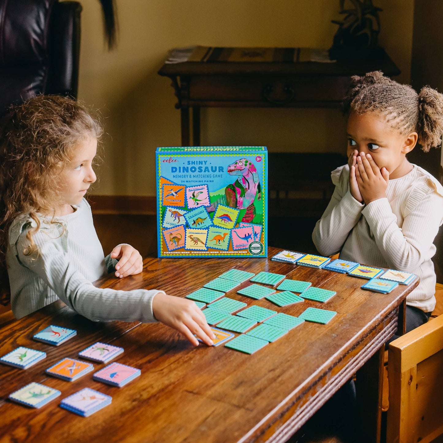 Two children playing a board game with colorful cards on a wooden table.