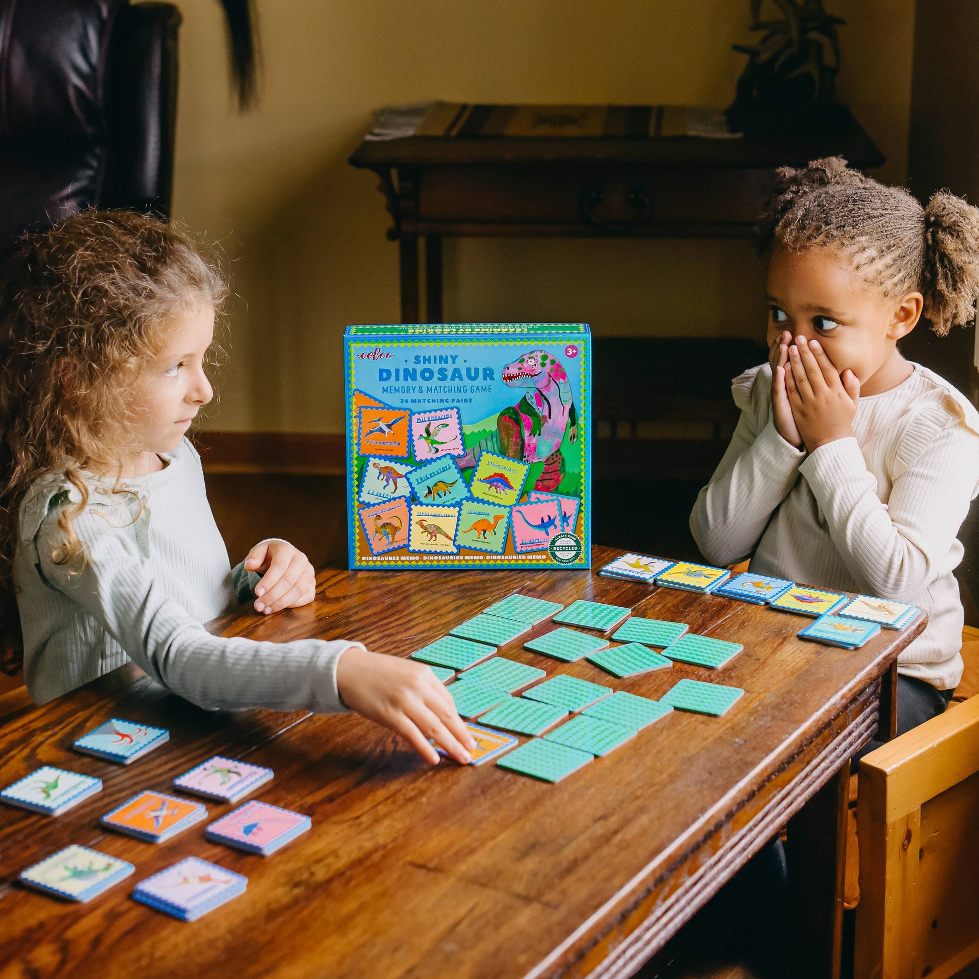 Two children playing a board game with colorful cards on a wooden table.