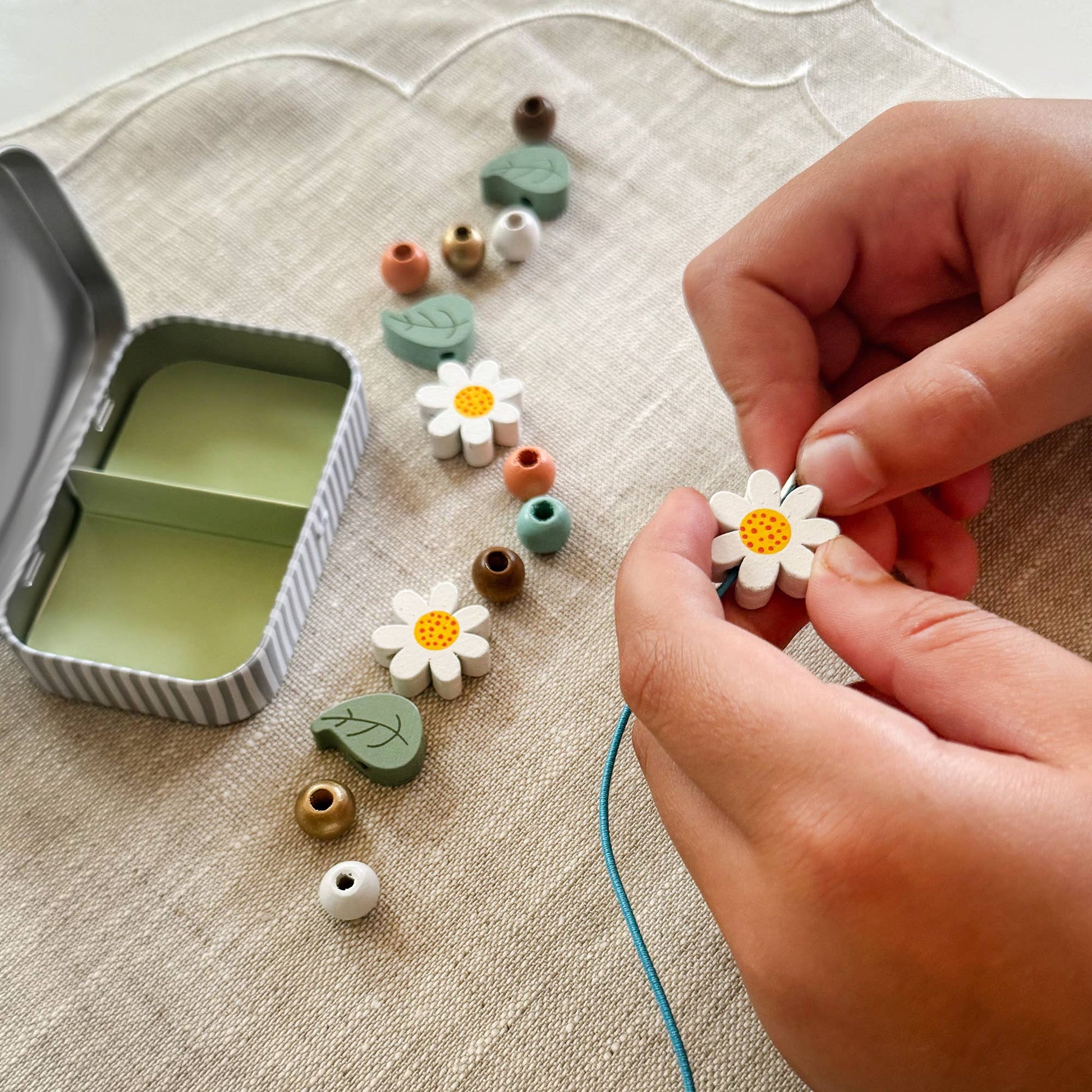 Person assembling flower-shaped beads on a textured surface with a small container.