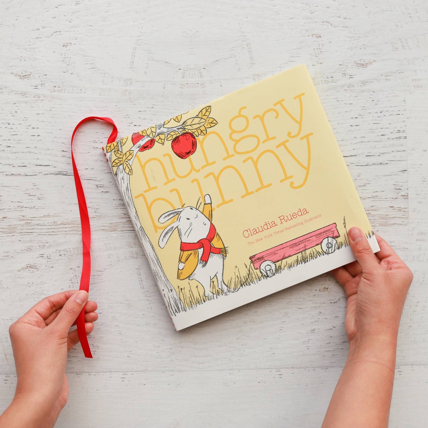 Children's book titled 'Hungry Bunny' held by hands on a light wooden surface