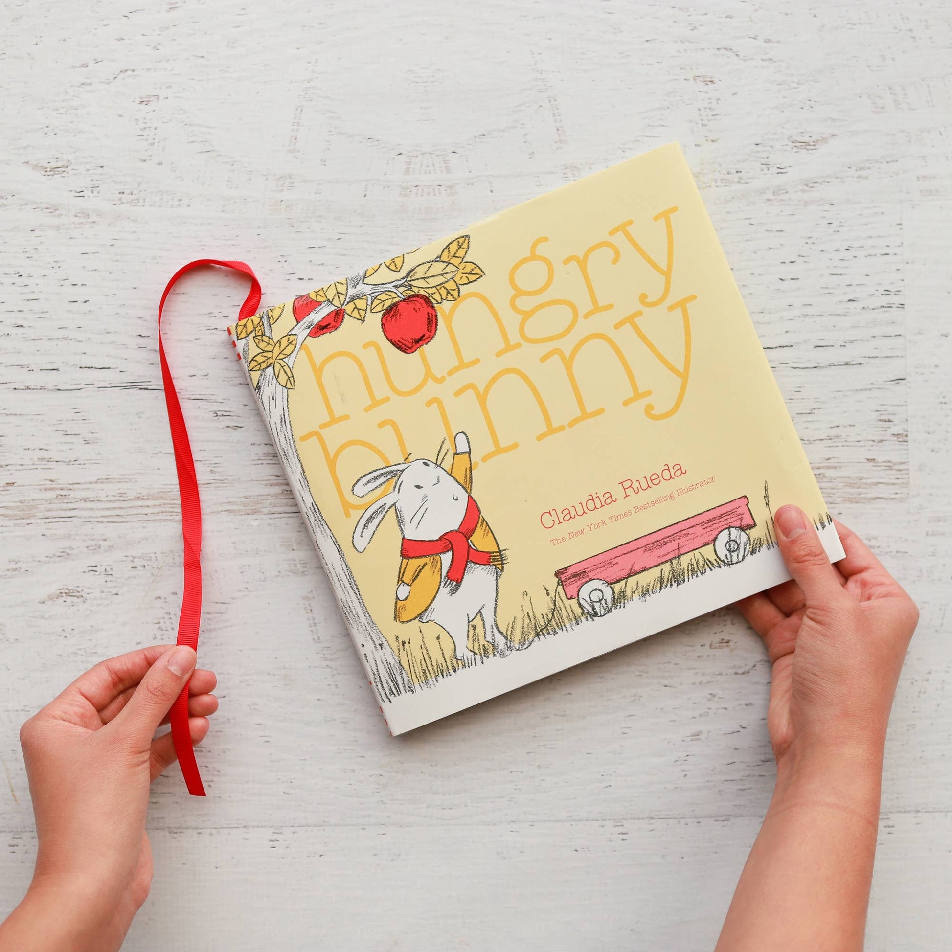 Children's book titled 'Hungry Bunny' held by hands on a light wooden surface