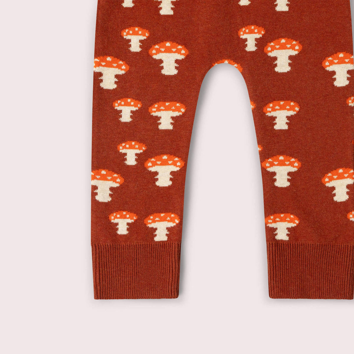 Close-up of mushroom motifs and ribbed ankle cuffs on rust knitted joggers.
