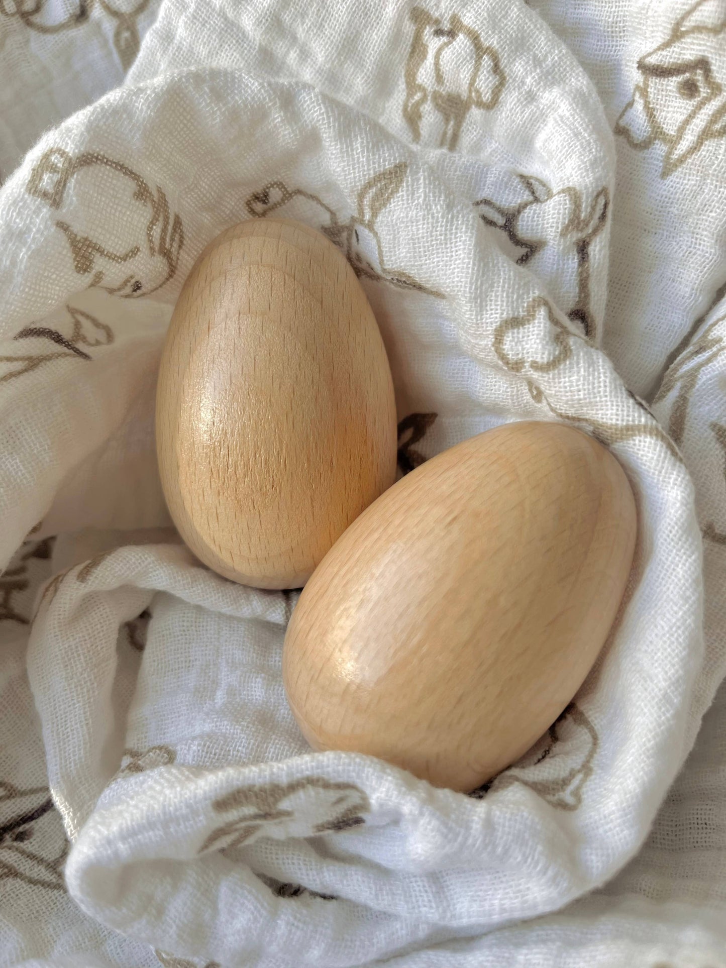 Two wooden eggs on a white cloth with animal prints