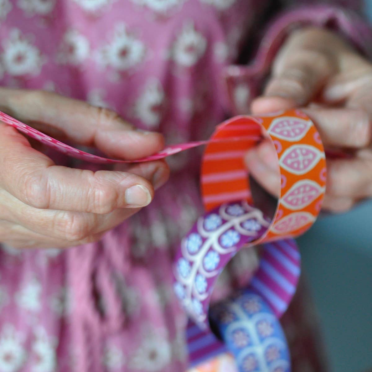 Close-up of hands looping an orange patterned paper strip into a colorful paper chain.
