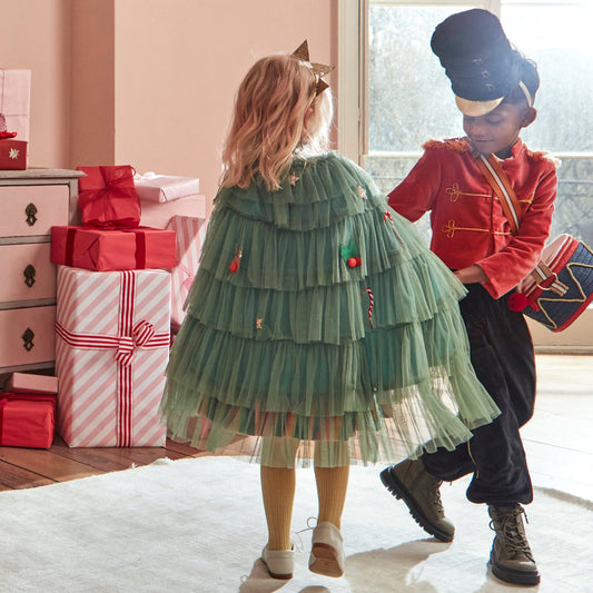Two children in festive outfits standing in a room with Christmas decorations.