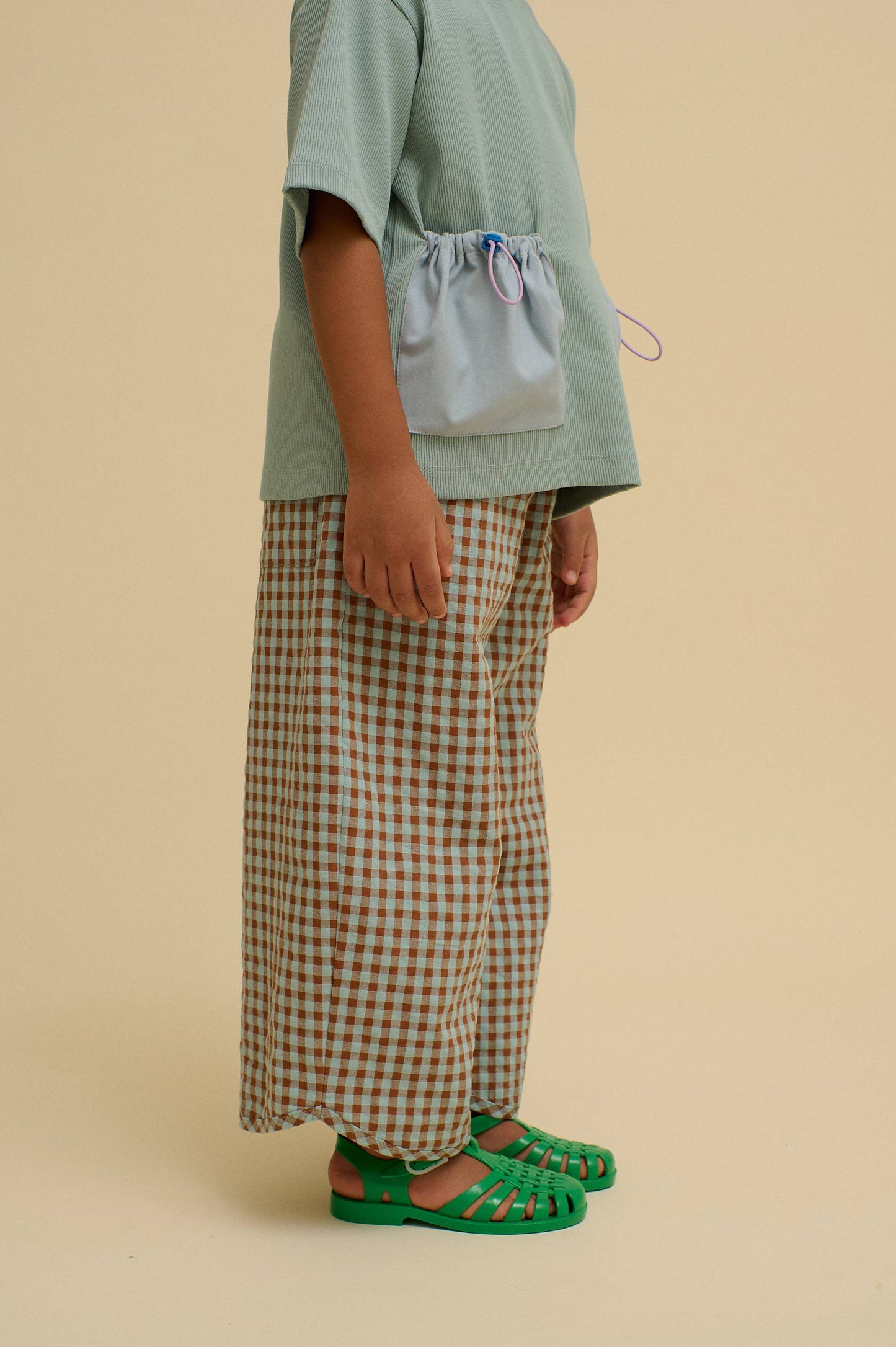Child wearing a green top and checkered pants on a beige background