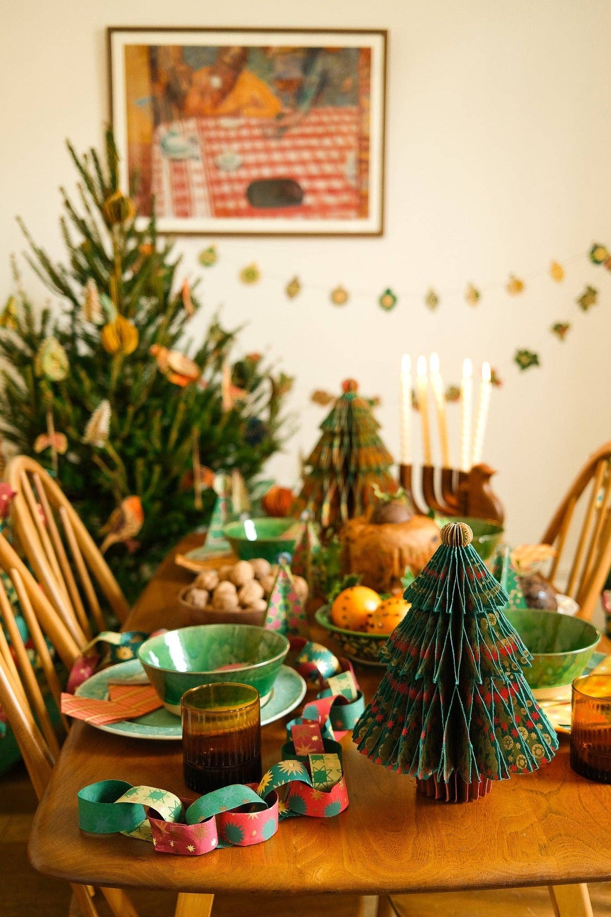 Christmas dining table decorated with festive paper chains, green honeycomb trees and green tableware.