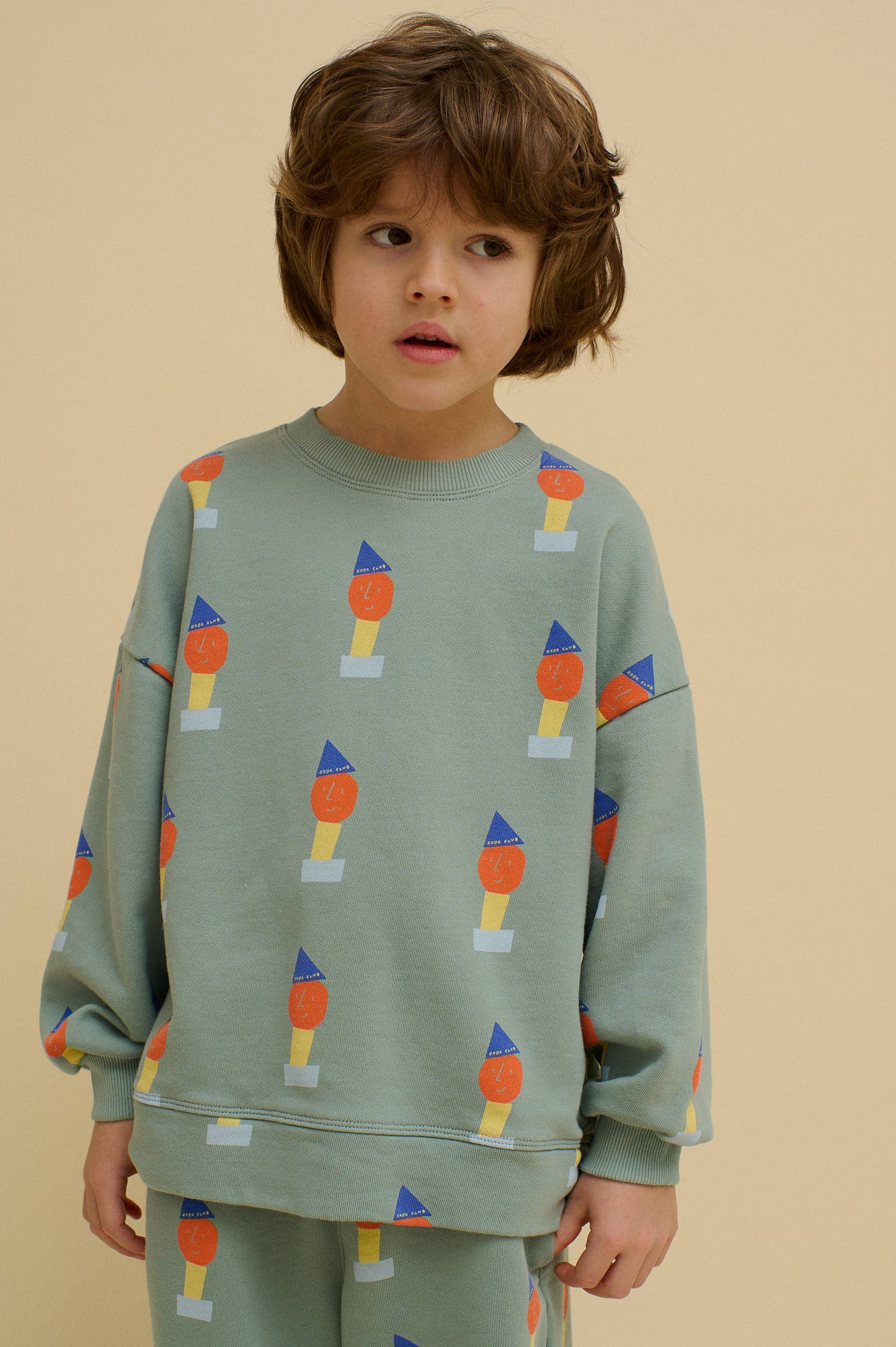 Child wearing a green sweatshirt with colorful pattern on a beige background