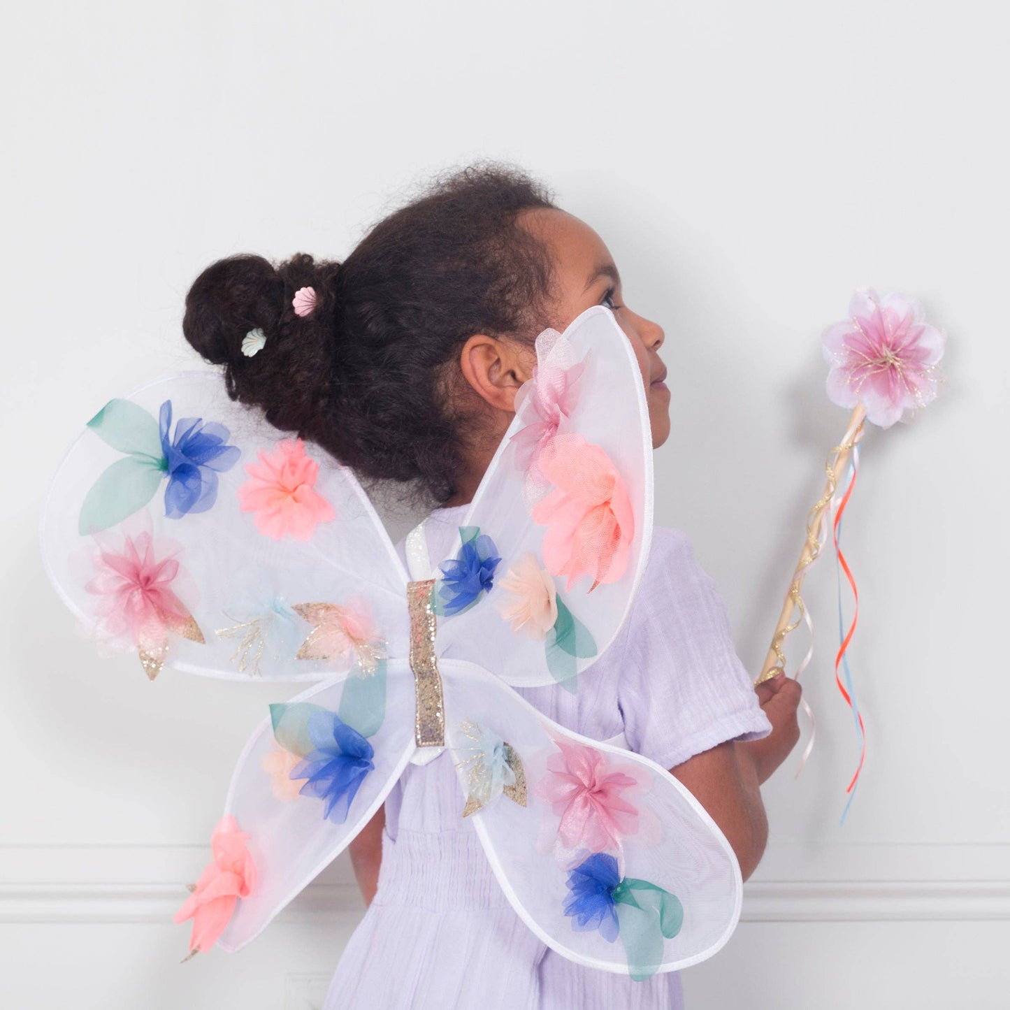 Child wearing colorful fairy wings and holding a wand against a white background