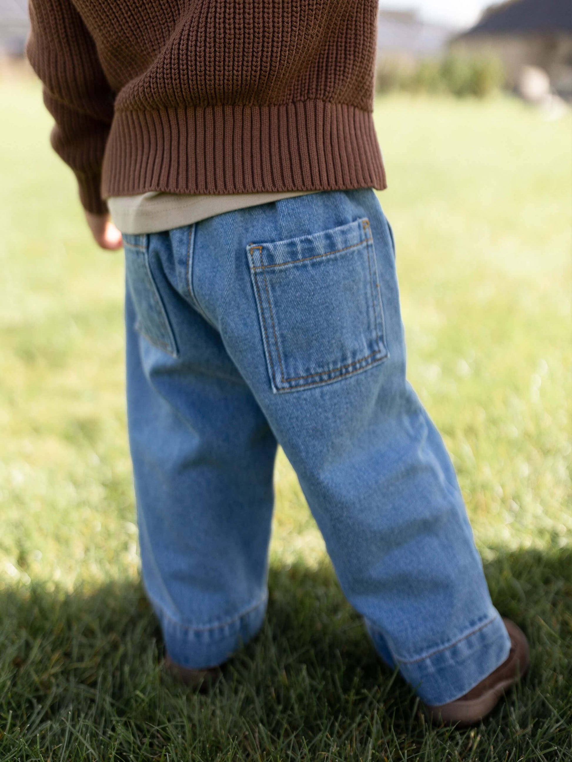 Child wearing blue jeans and a brown sweater standing on grass