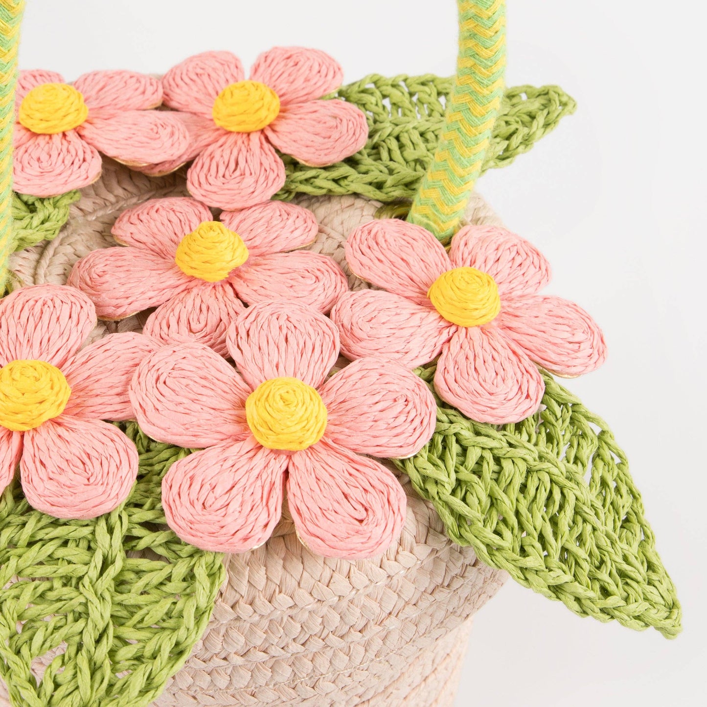 Close-up of a woven bag with pink floral patterns and green leaves on a white background