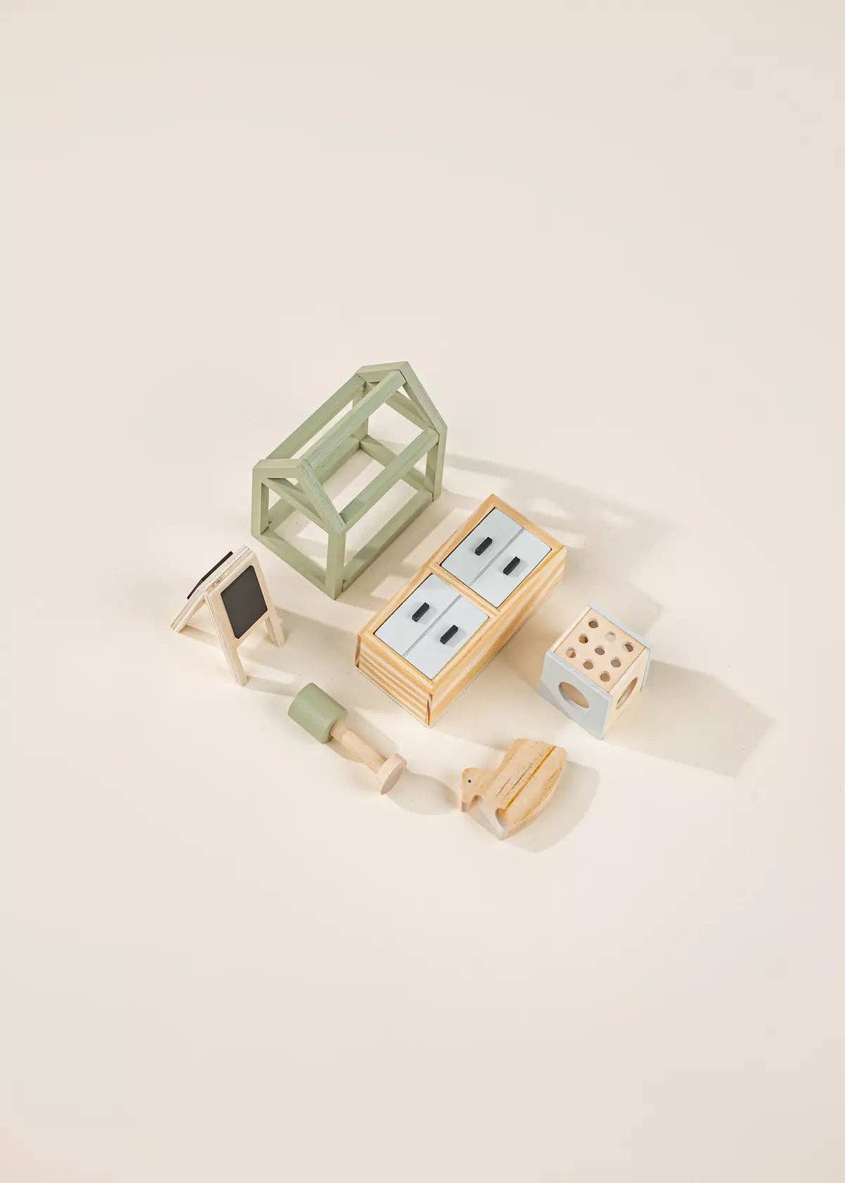 Set of wooden dollhouse toys including a house bed, a dresser, an easel, and a lamp on a beige background