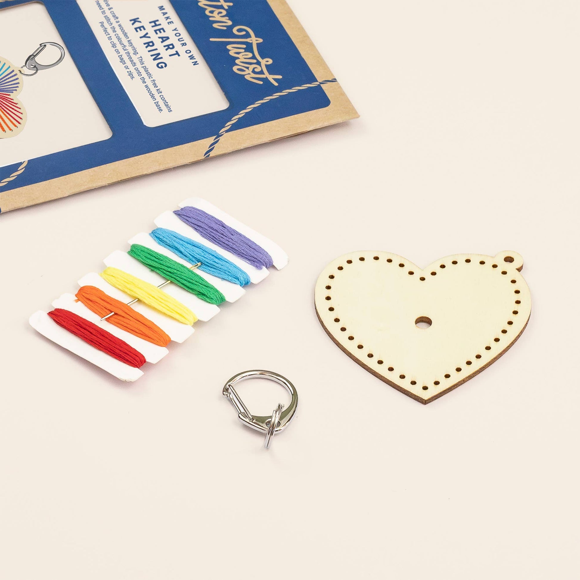 Heart-shaped keyring kit with colorful strings, wooden heart template, and metal keyring on a light background.
