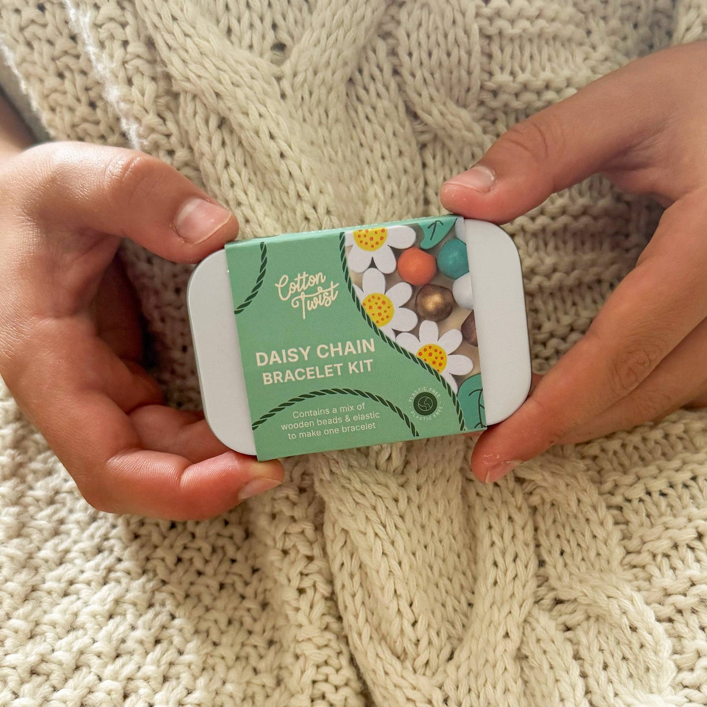 Person holding a 'Daisy Chain Bracelet Kit' against a knitted fabric background