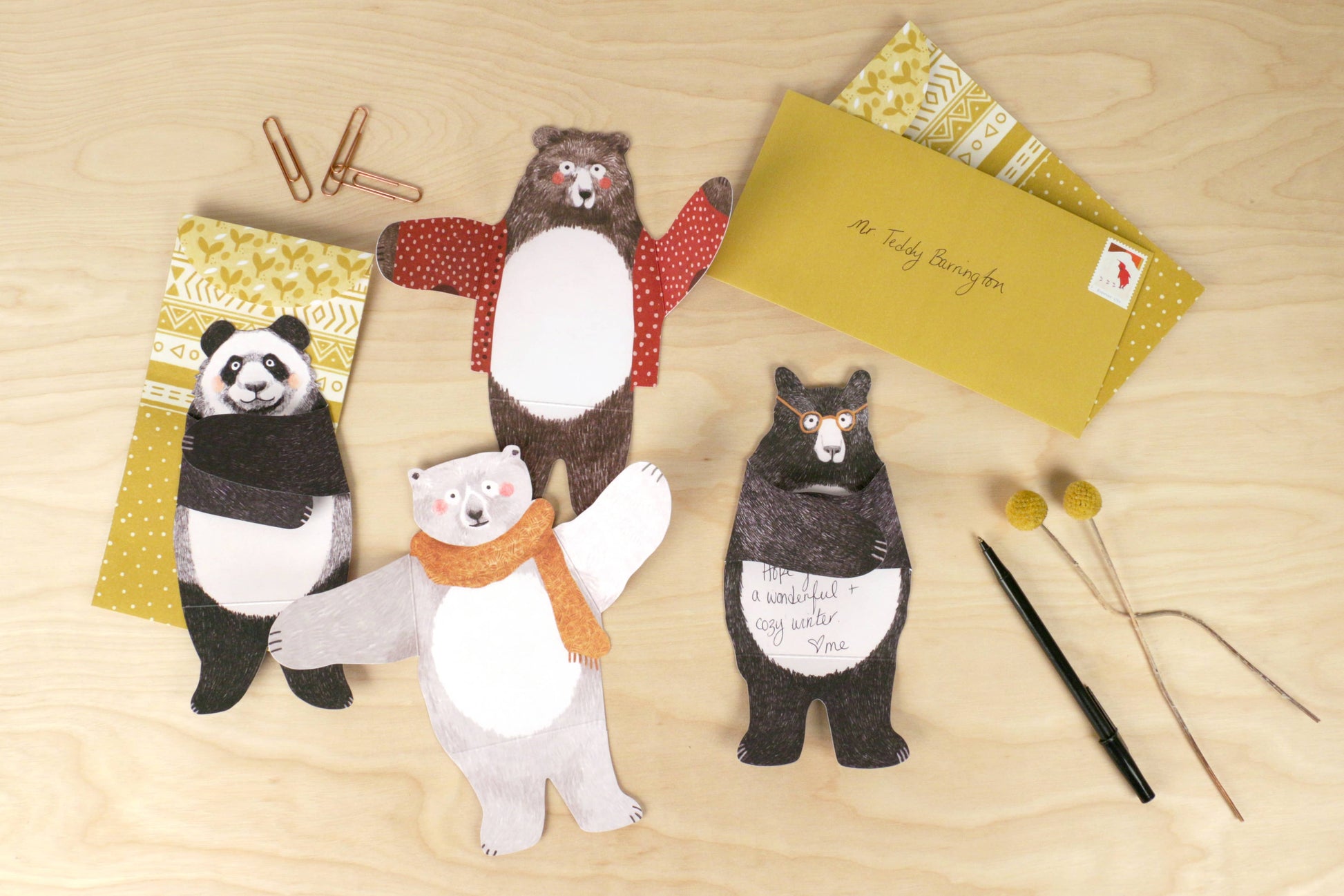 Four bear-shaped cards with scarves on a wooden surface