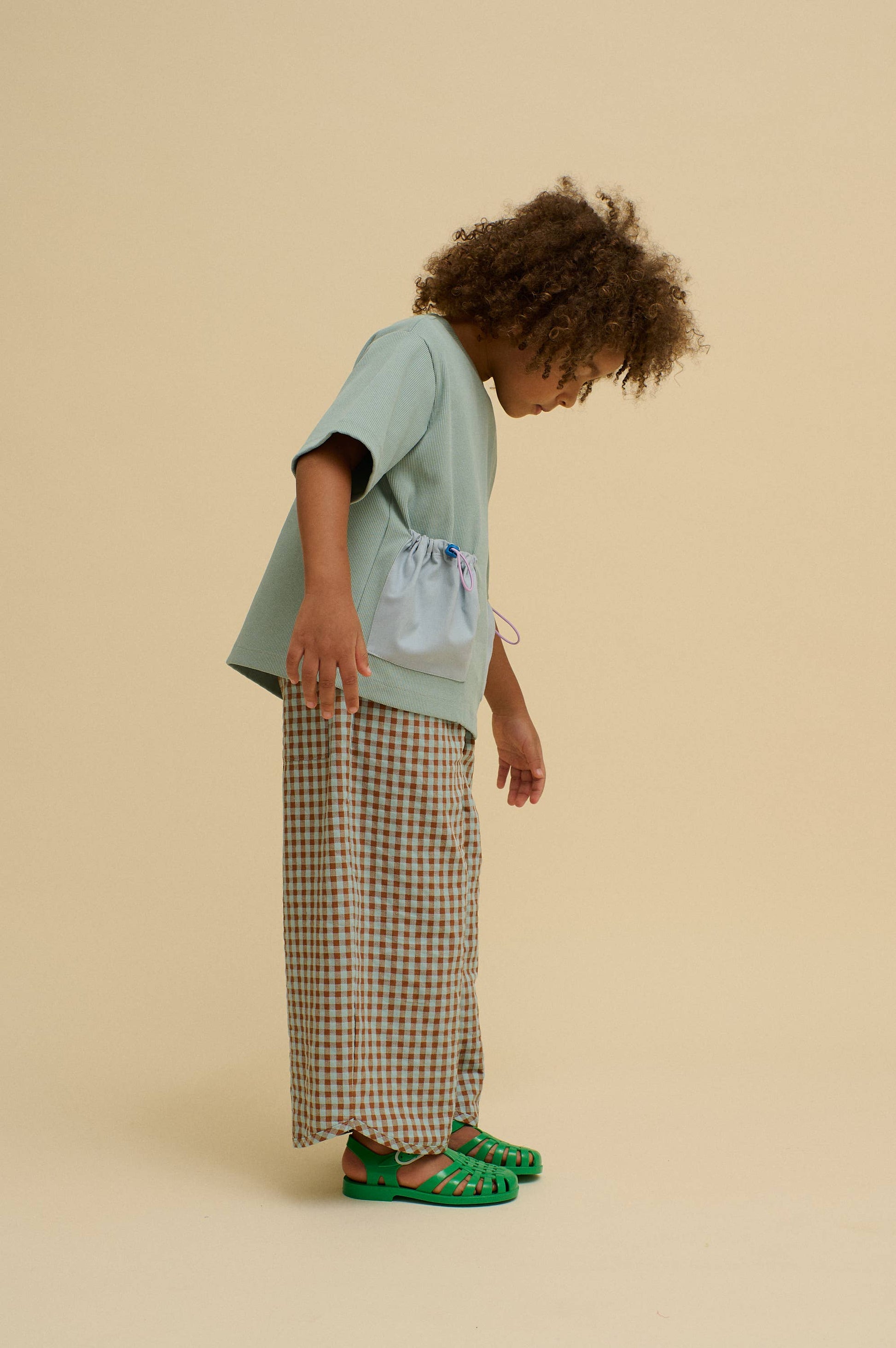 Child wearing a light green shirt and plaid pants on a beige background
