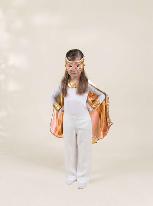 Child wearing a superhero costume with a gold cape and mask on a plain background
