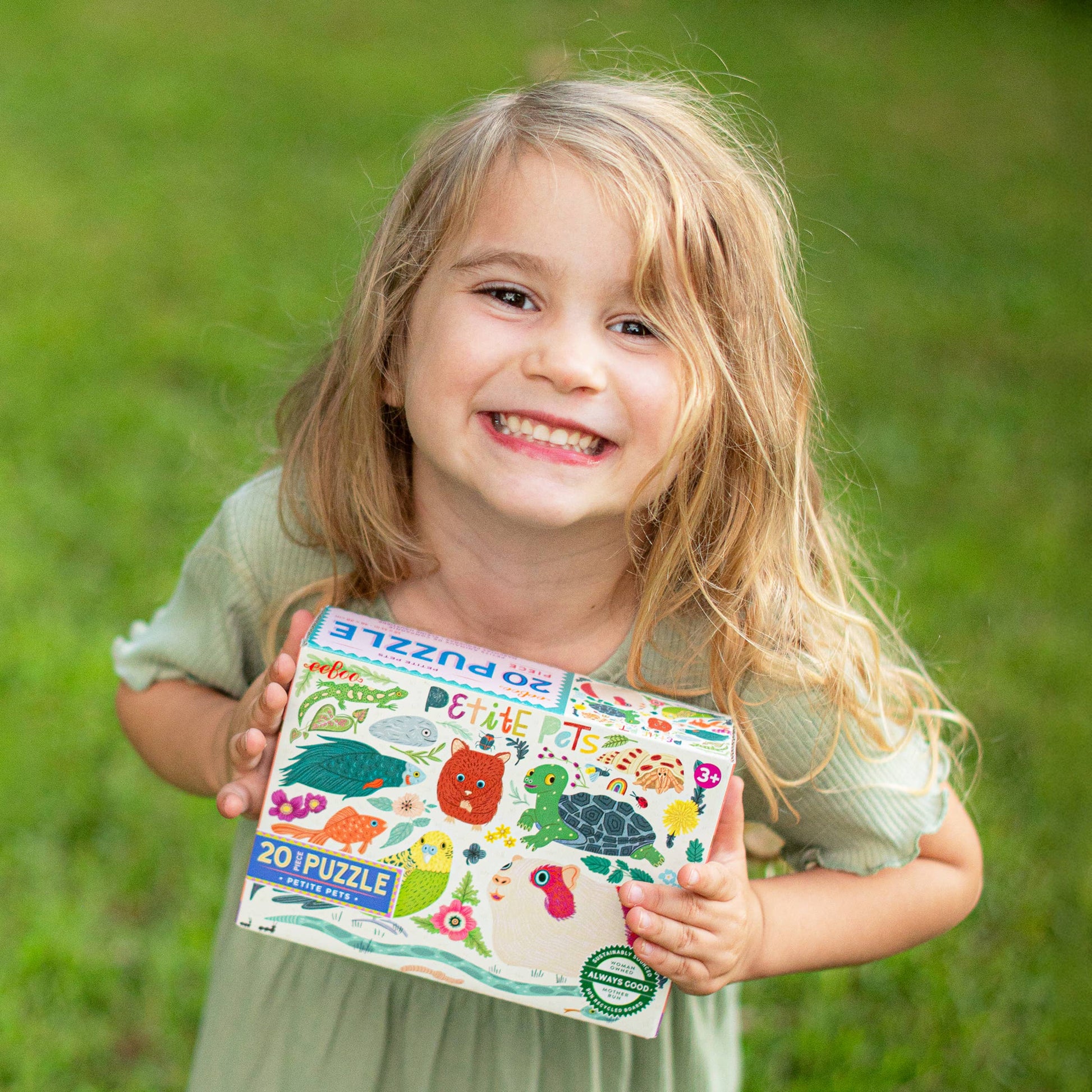 Child holding a children's puzzle book outdoors on grass