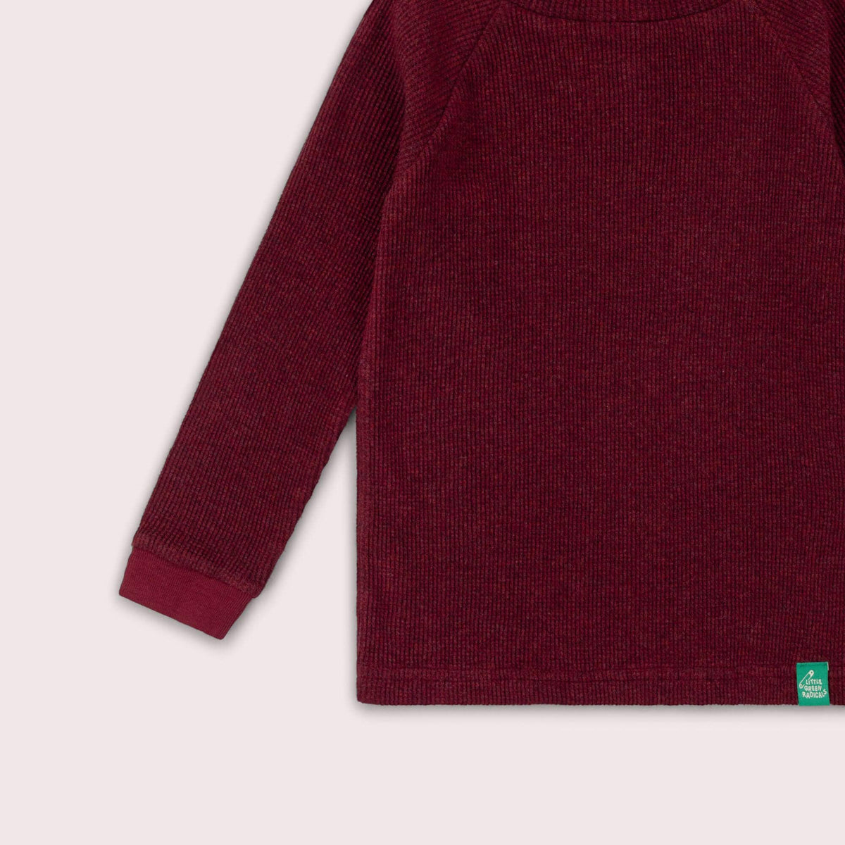 Detail of the ribbed cuff, hem and green label on a burgundy waffle top.