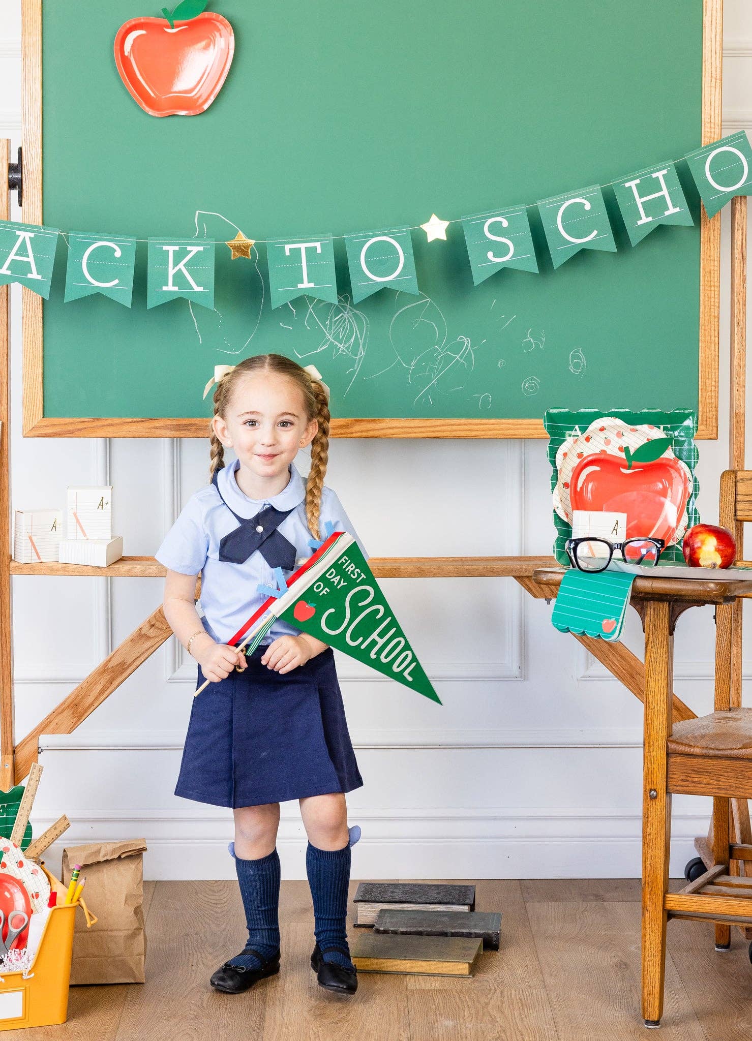 Child holding green “first day of school” pennant in a classroom setting