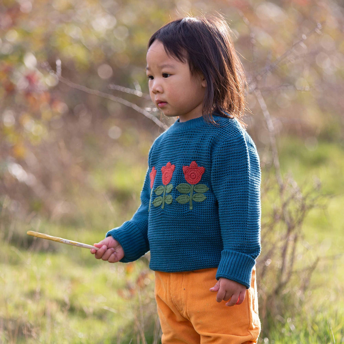 Child wearing a teal knitted jumper with three red tulips outdoors.