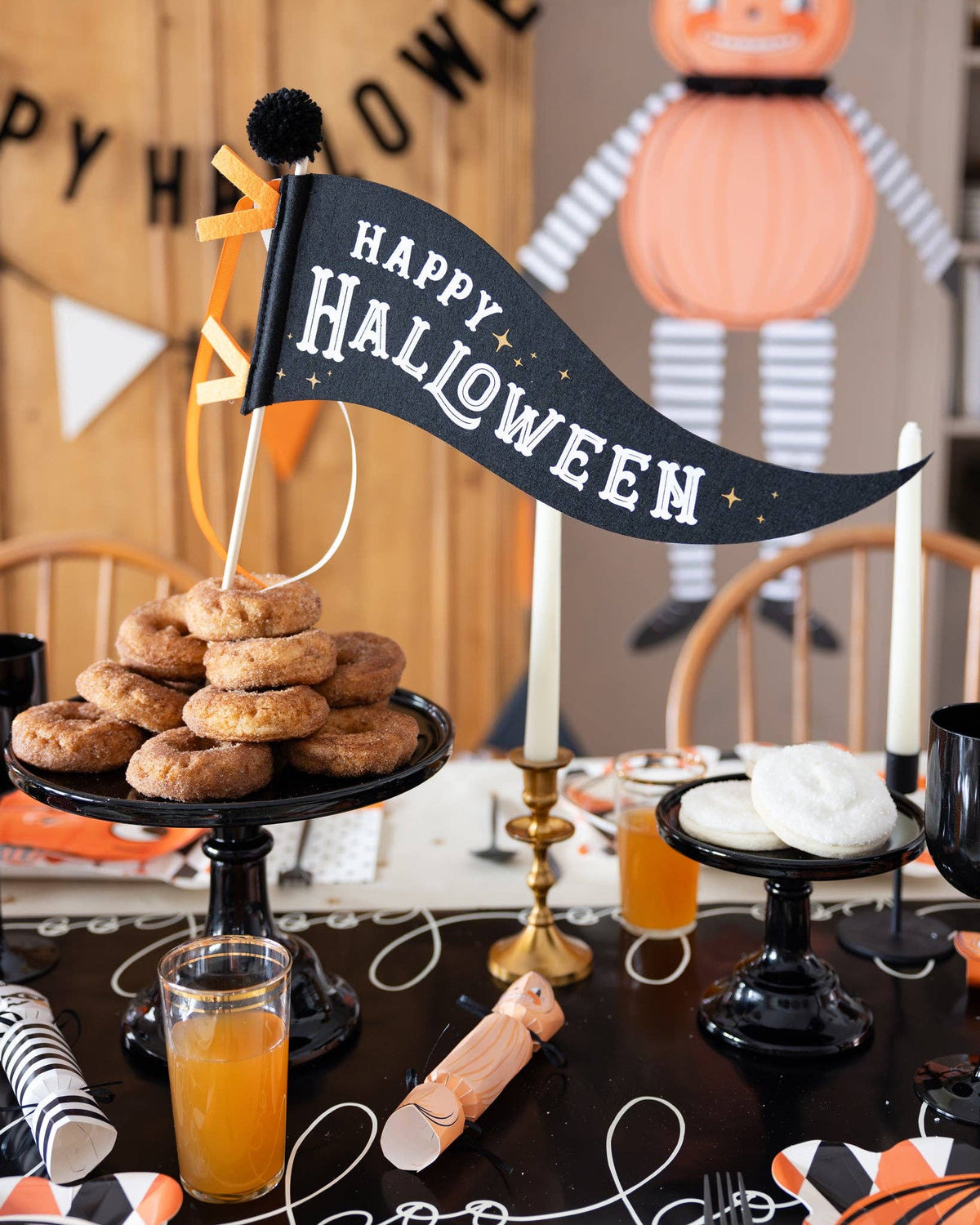 Halloween-themed table setting with 'Happy Halloween' banner, donut tower, and pumpkins.
