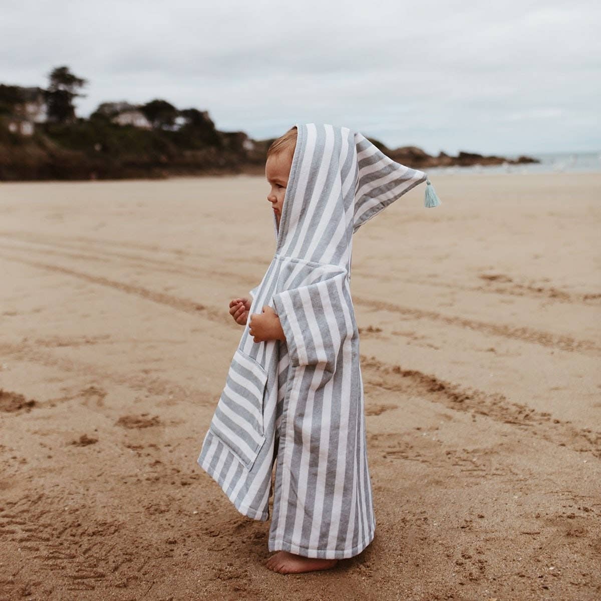 Child wrapped in a striped towel on a sandy beach