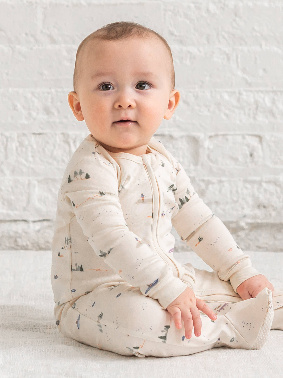 Baby wearing a white onesie with small patterns sitting on a white surface.
