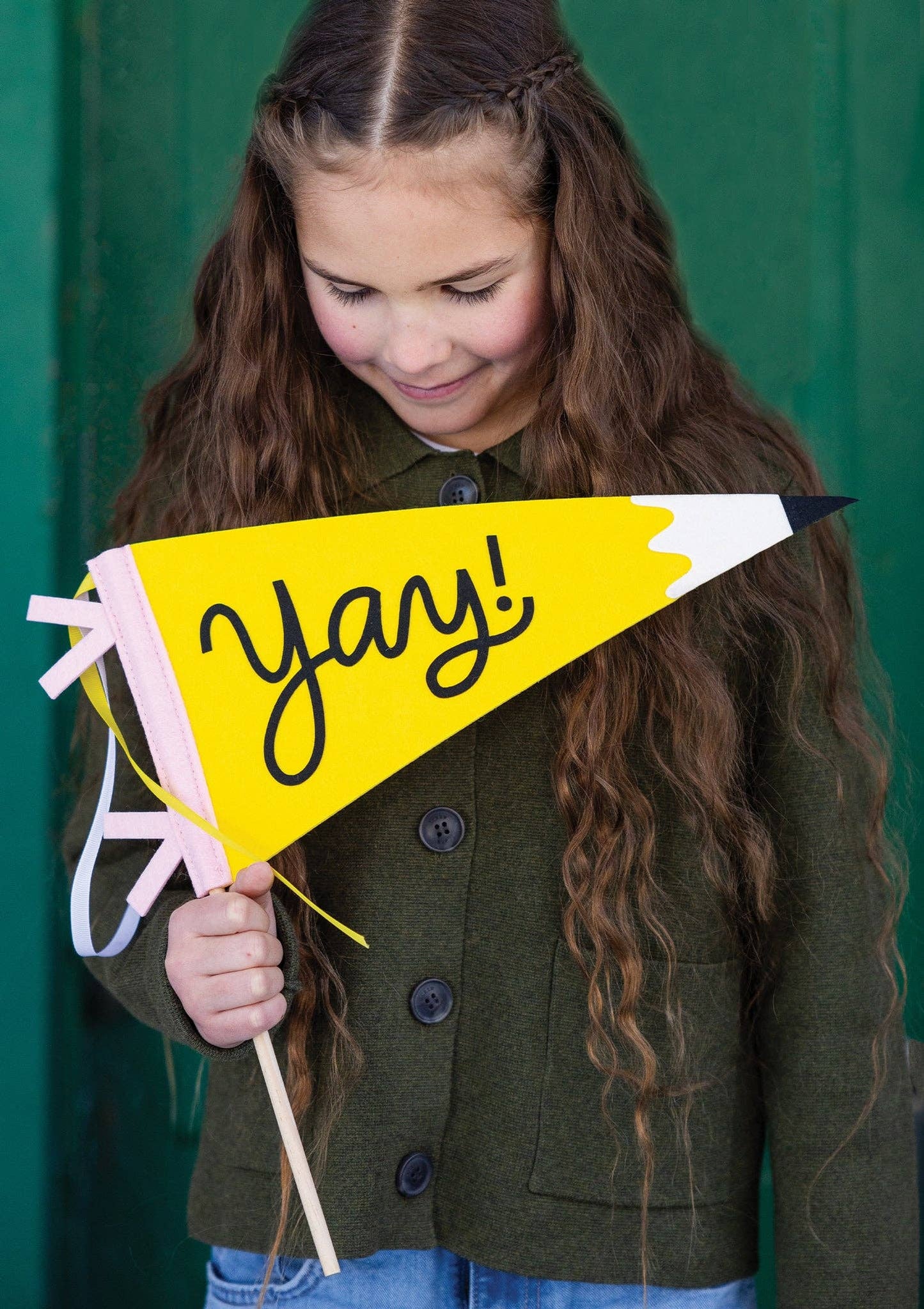 Child wearing a green coat, holding a Yay pennant