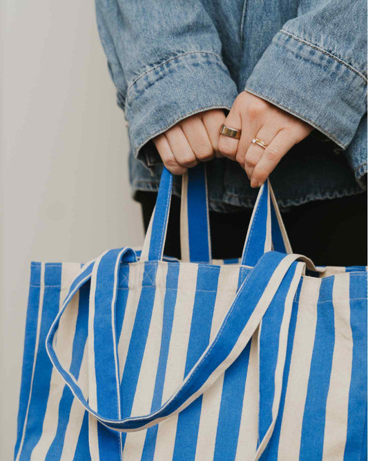 Person holding a blue and white striped tote bag with a neutral background