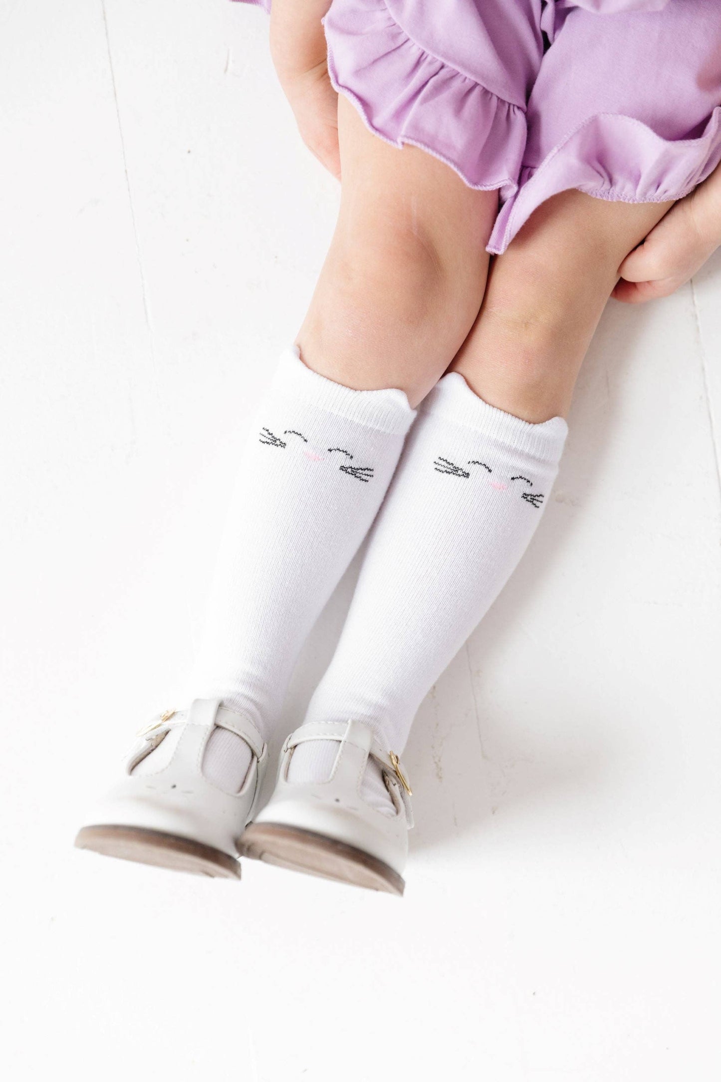 Child wearing white knee-high socks with animal prints and white shoes on a white background