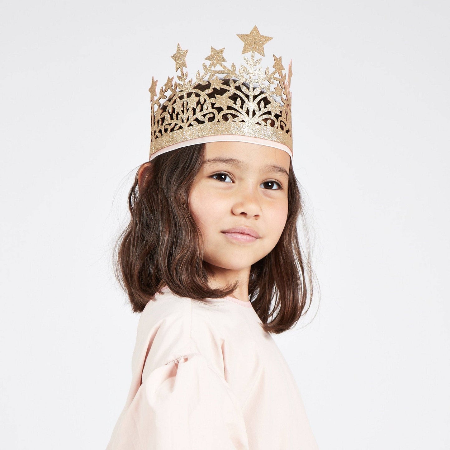 Young girl wearing a gold star-patterned crown on a white background