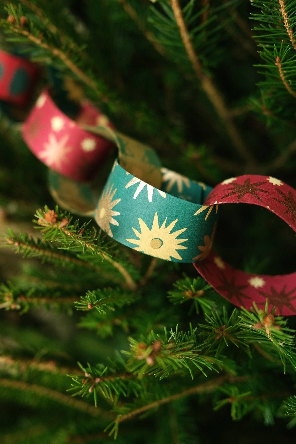 Close-up of red and green paper chain links with gold sunburst patterns on a Christmas tree.