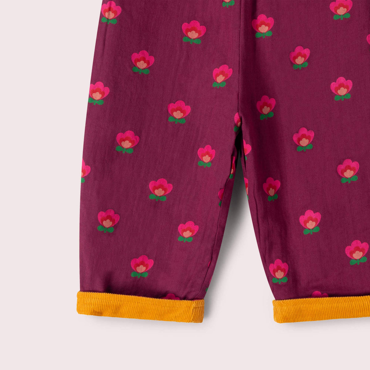 Close-up of pink floral print and mustard turned-up cuffs on purple reversible trousers.