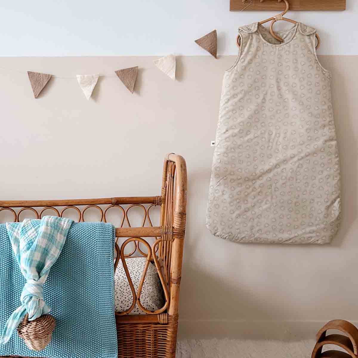 Baby sleeping bag hanging on a hook next to a wicker chair with a blue blanket