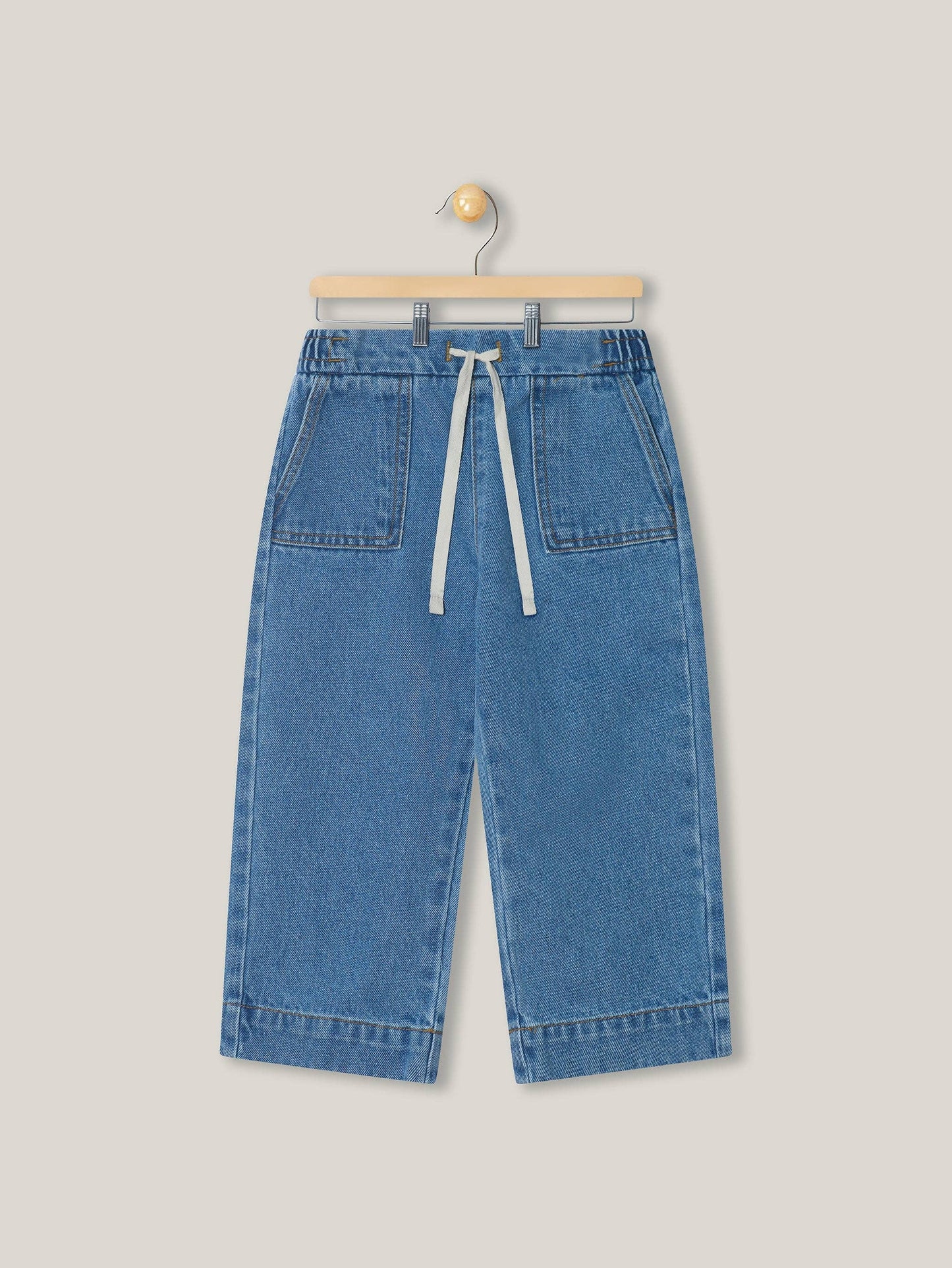 Blue denim pants on a hanger against a light gray background