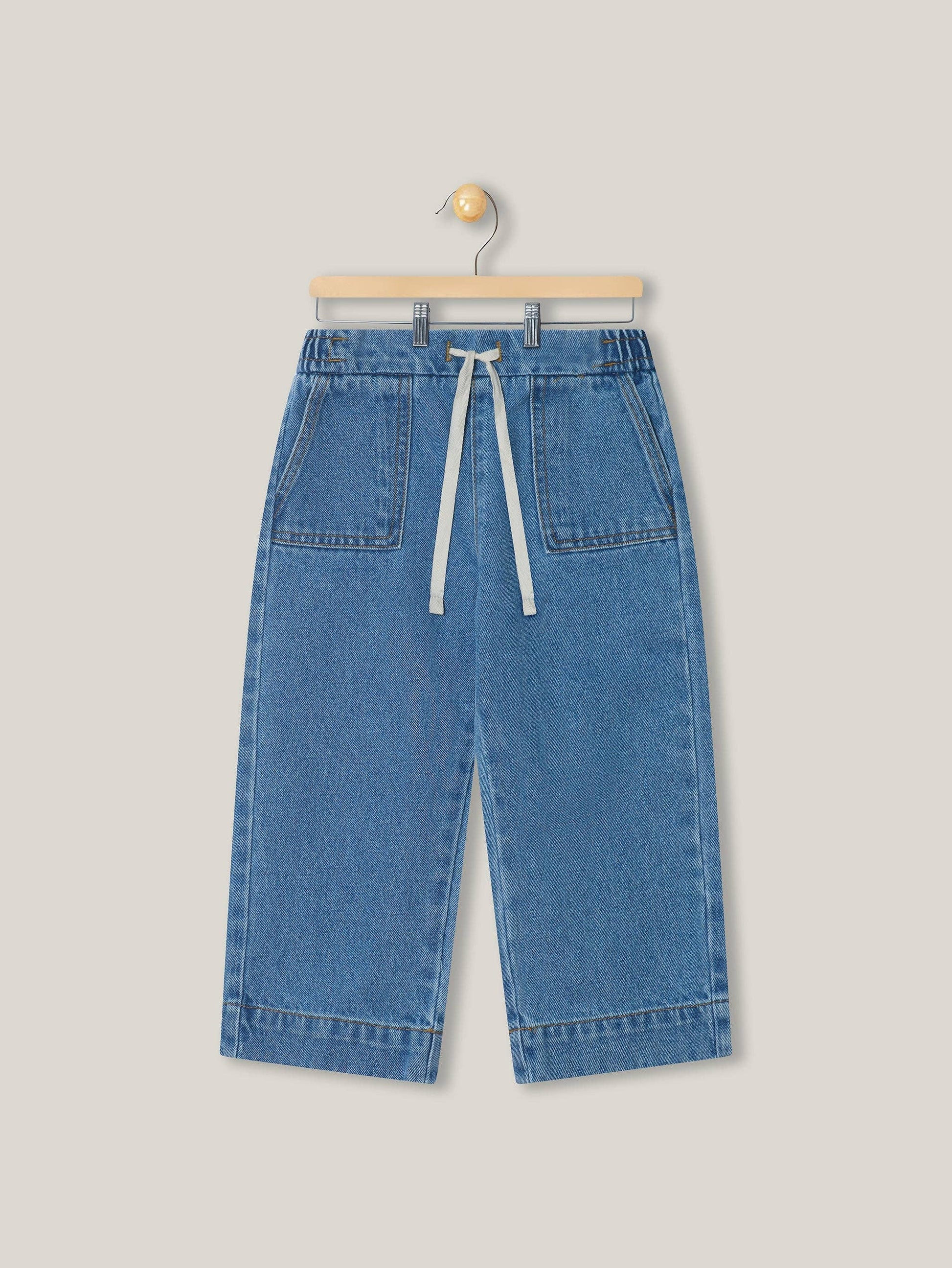 Blue denim pants on a hanger against a light gray background