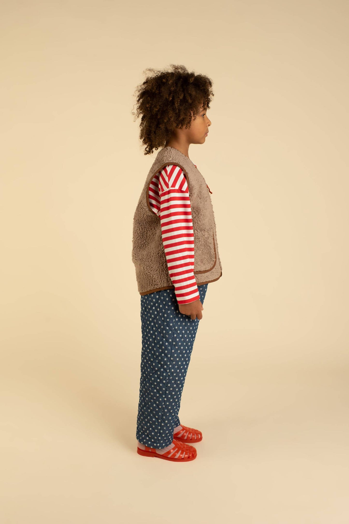 Child wearing a striped shirt, patterned pants, and a jacket on a beige background