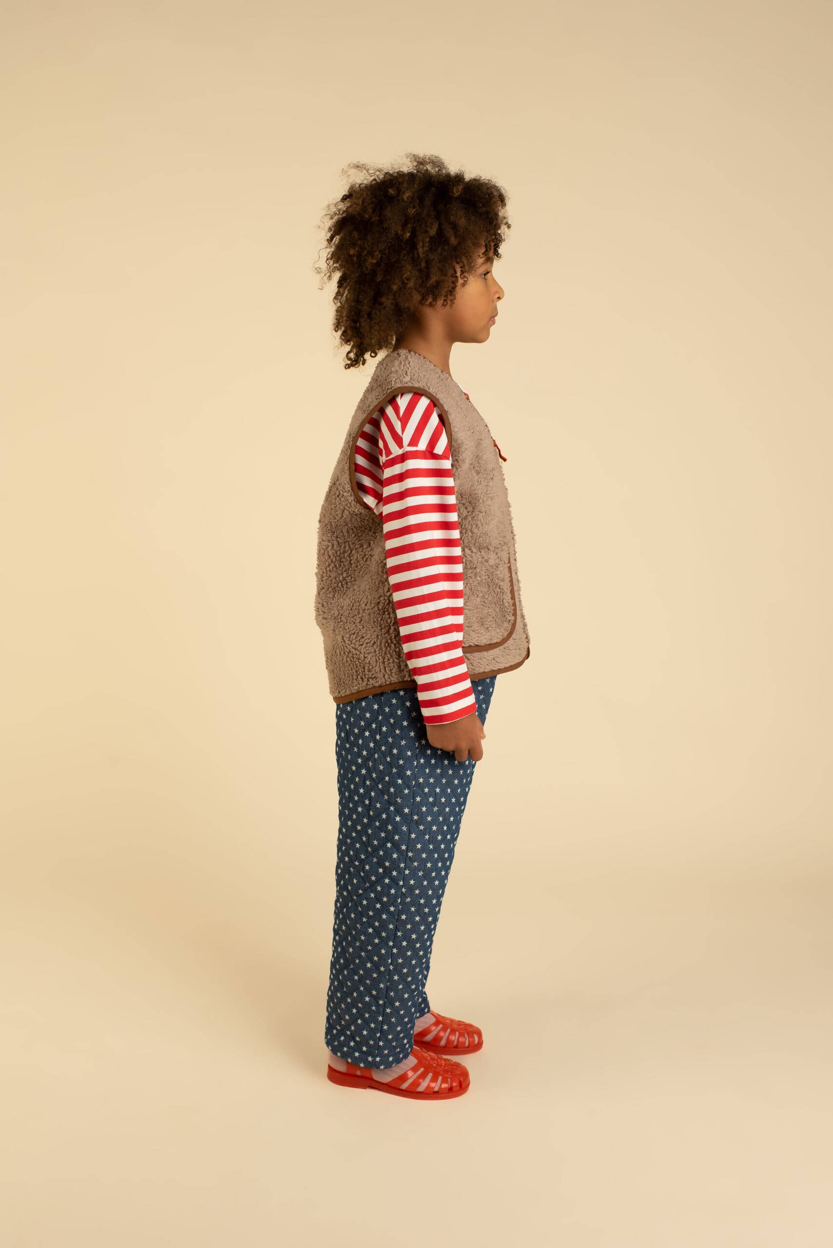 Child wearing a striped shirt, patterned pants, and a jacket on a beige background