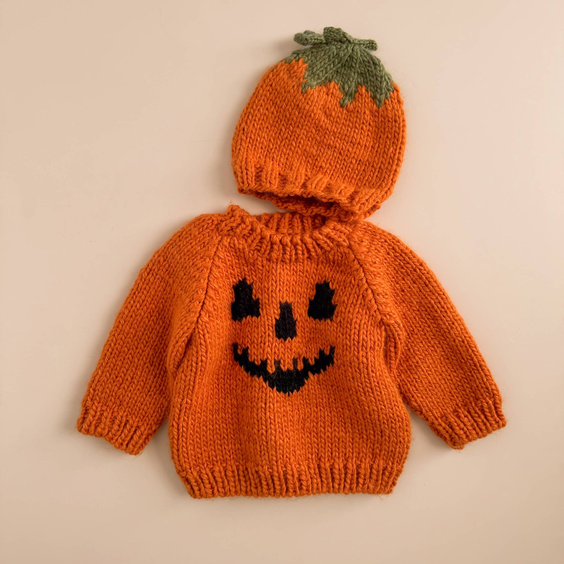 Knitted sweater and hat set designed like a pumpkin on a beige background