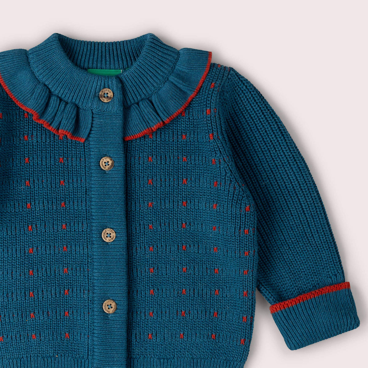 Close-up of the frilled collar, buttons and red-edged cuff on a teal knitted cardigan.