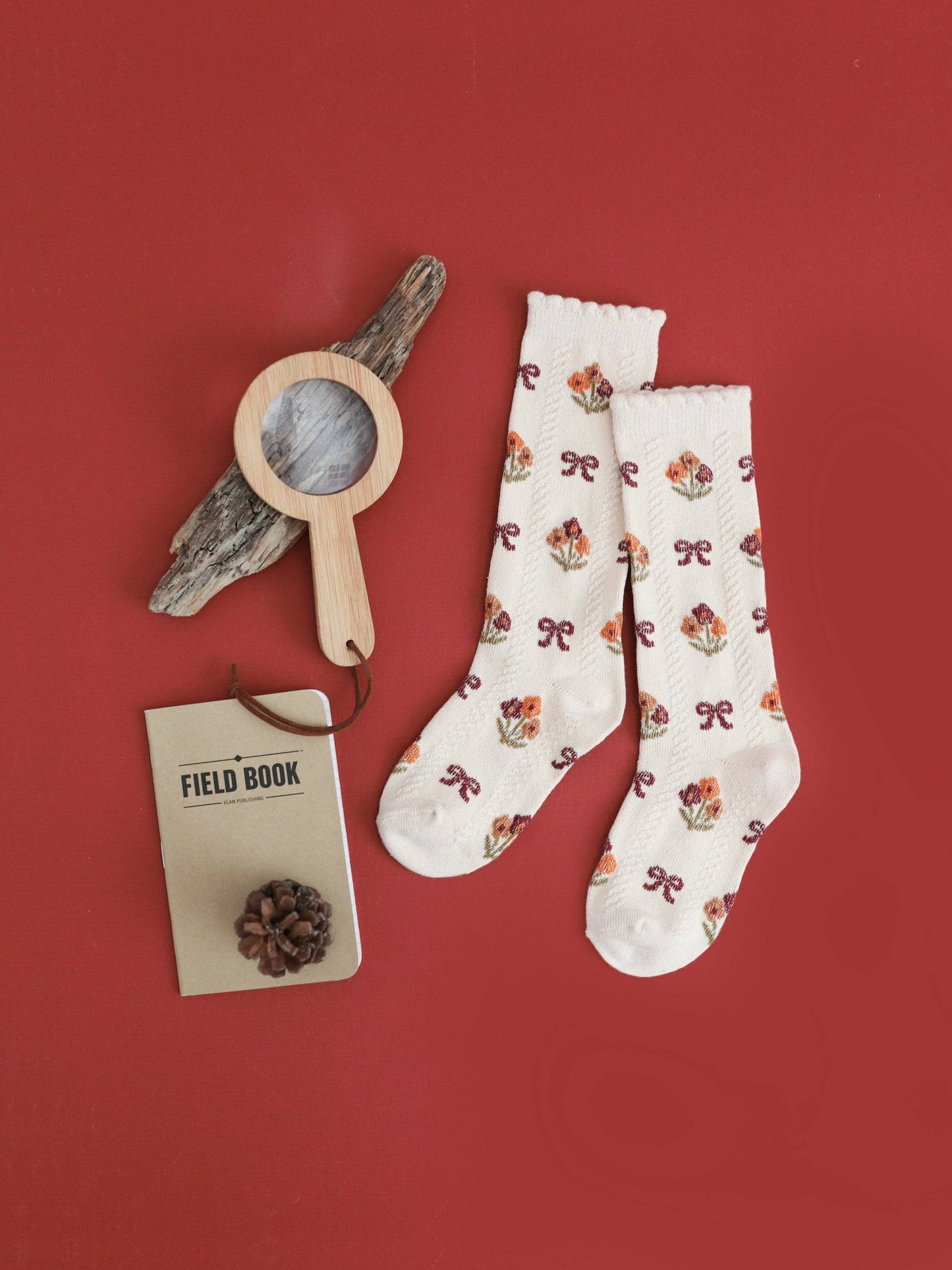 White socks with floral patterns on a red background, accompanied by a wooden tool and field book.