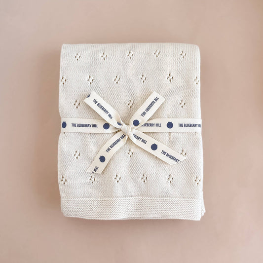 cotton embroidered cream-colored baby blanket folded and tied with ribbon on a beige background