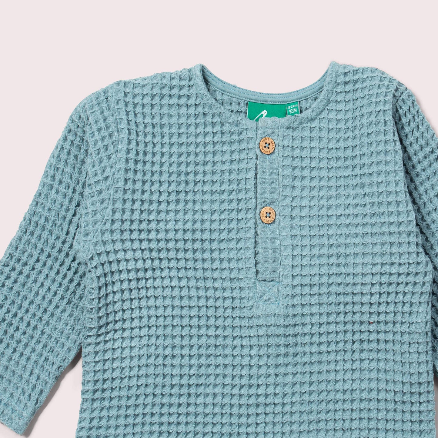 Light blue textured cardigan with buttons on a light pink background
